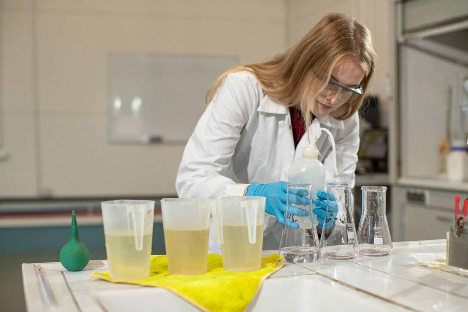 Kobieta w laboratoryjnym fartuchu przeprowadza eksperyment, nalewając ciecz do kolb i używając przyrządów chemicznych