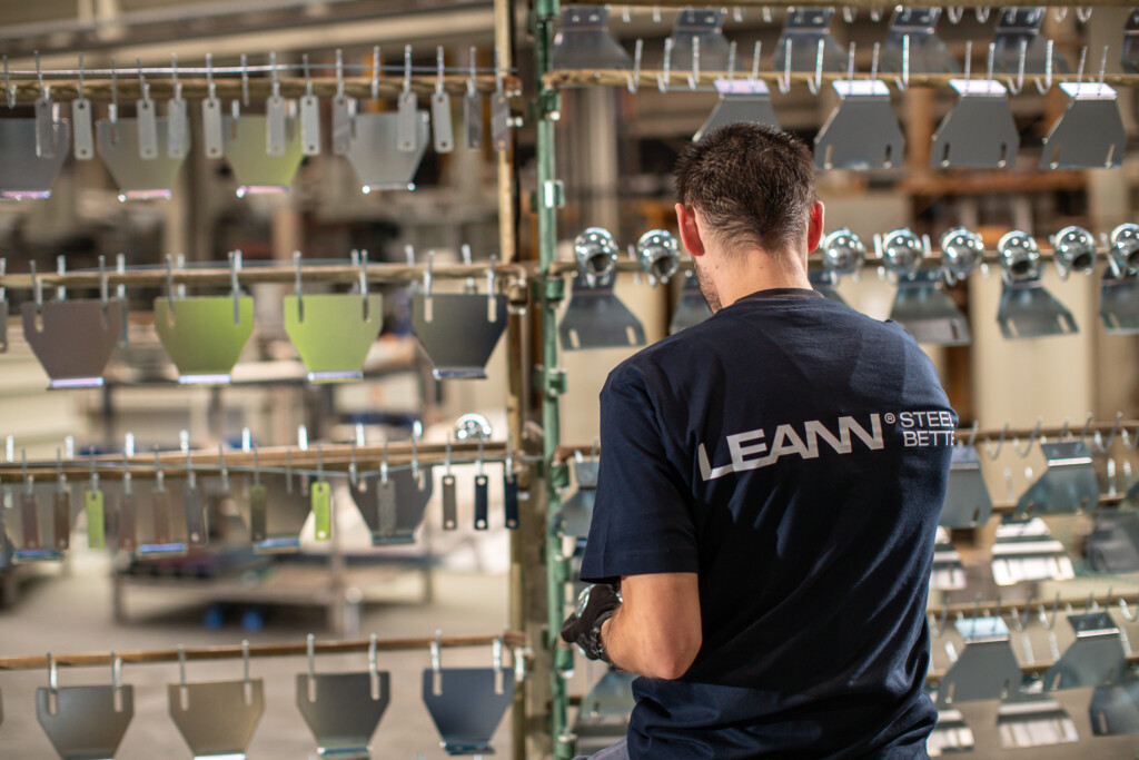 Pracownik w warsztacie LEANN, zajmujący się stalowymi konstrukcjami, obok wieszaka z metalowymi elementami do produkcji