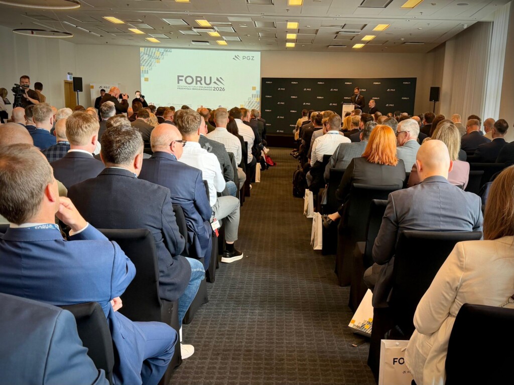 Tłumna sala konferencyjna, uczestnicy siedzą na krzesłach, na scenie prelegent z prezentacją na ekranie
