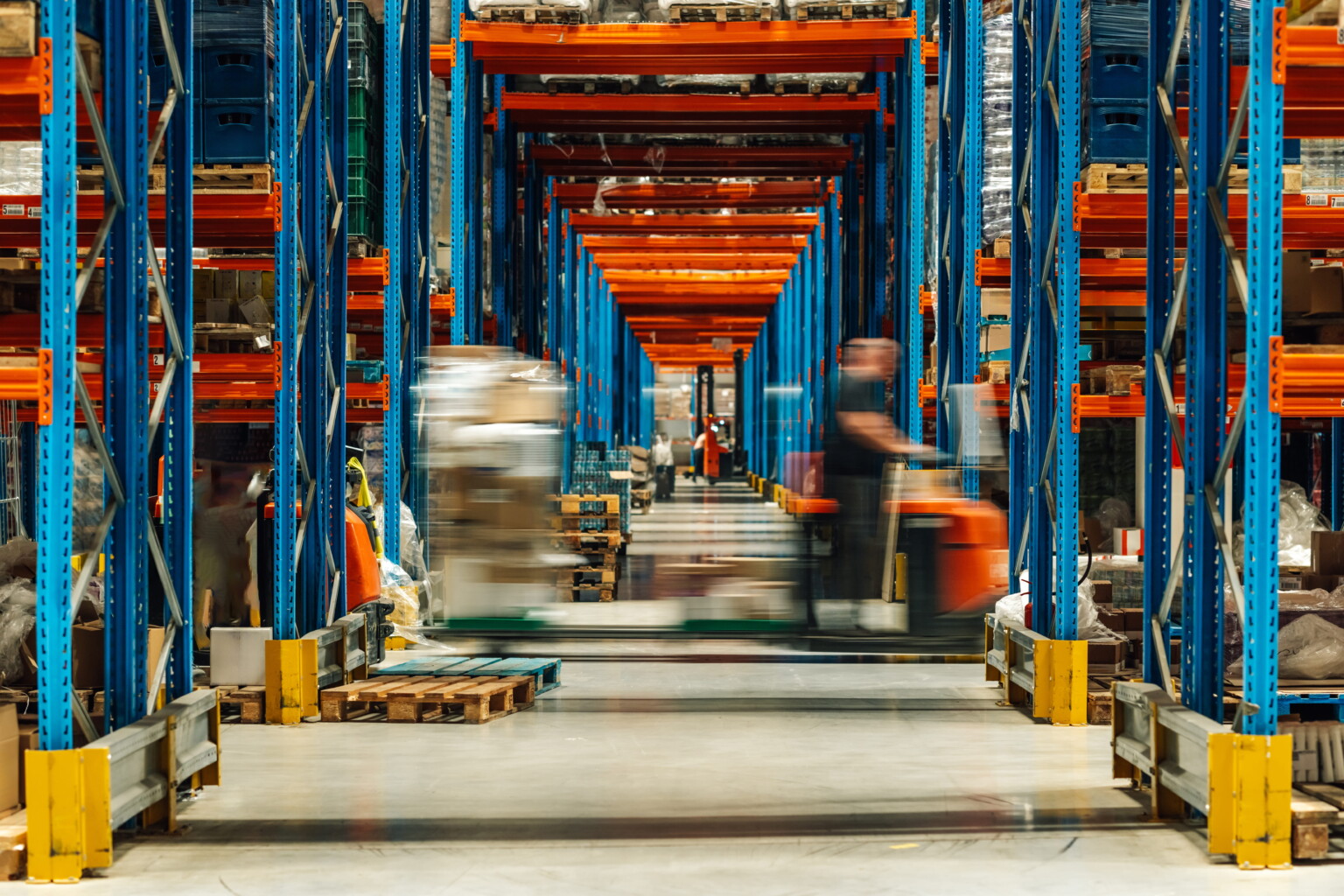 Cargo w magazynie z regałami w niebiesko-pomarańczowych kolorach i poruszającymi się wózkami transportowymi
