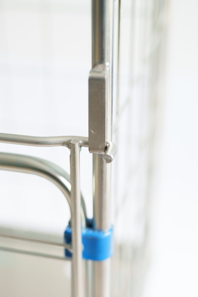 Zbliżenie na metalowy stelaż z zatrzaskiem i niebieską opaską na łączeniu rur Rollkontenera HYGIENE Access