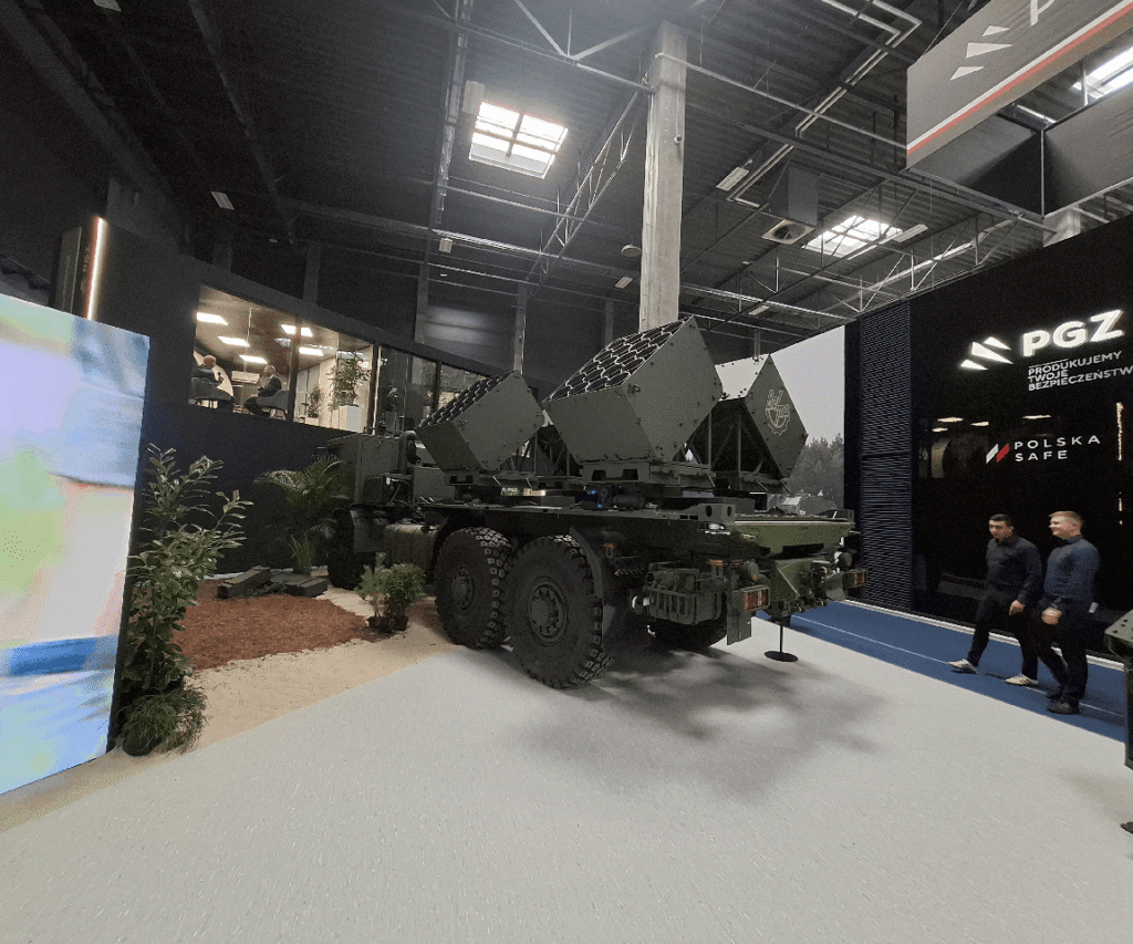 Model militarnego pojazdu na wystawie, z widocznymi rakietami i osobami w tle, logo PGZ na ścianie